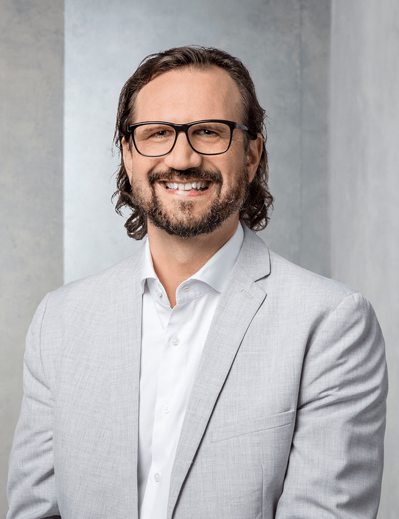 Mann stehend in hellem Anzug, der lächelt: Andreas Koller