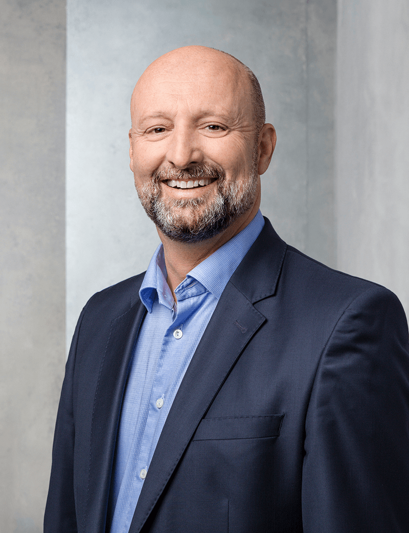 Mann stehend in dunklem Anzug, der lächelt: Daniel Rochat