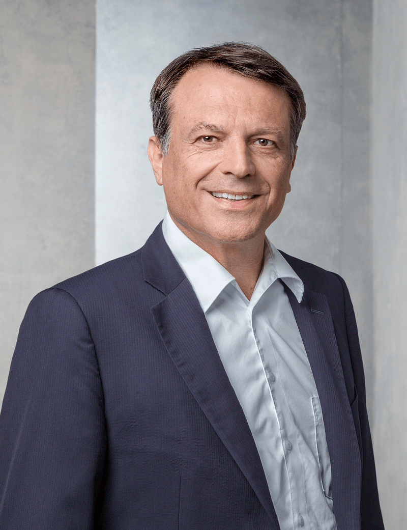 Mann stehend in dunklem Anzug, der lächelt: Norbert Reisinger